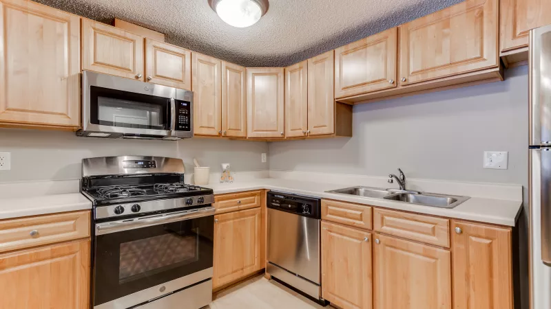 Kitchen with light wood cabinets, stainless steel oven, microwave, dishwasher, and refrigerator. Cream countertops.