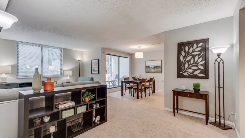 Open concept living and dining room with neutral decor, dark wood shelving unit, and balcony access.