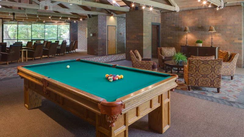 Billiard table in a well-lit recreation room with lounge seating, brick walls, and exposed wooden beams.