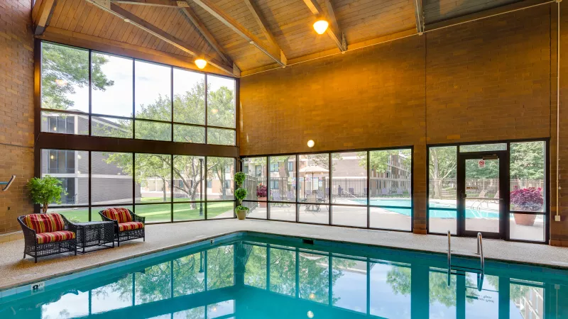 Spacious indoor swimming pool room with vaulted ceilings and large windows revealing an outdoor pool and landscaped grounds.